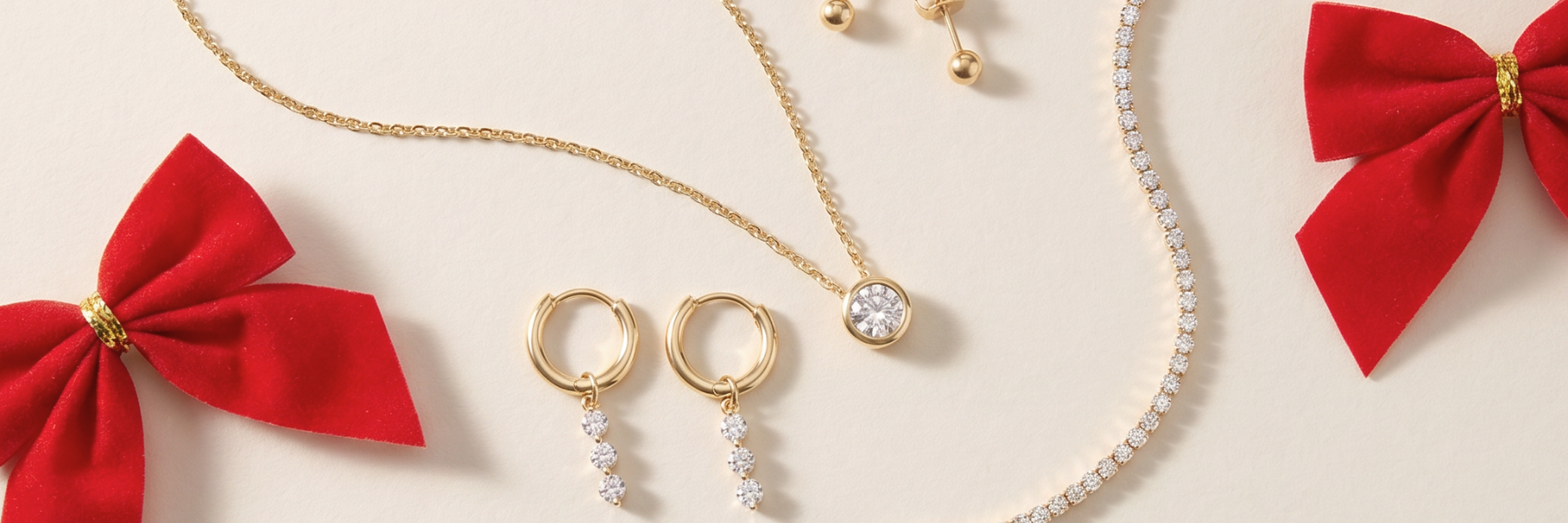 gold necklaces, hoops, and studs styled with red velvet bows for Christmas