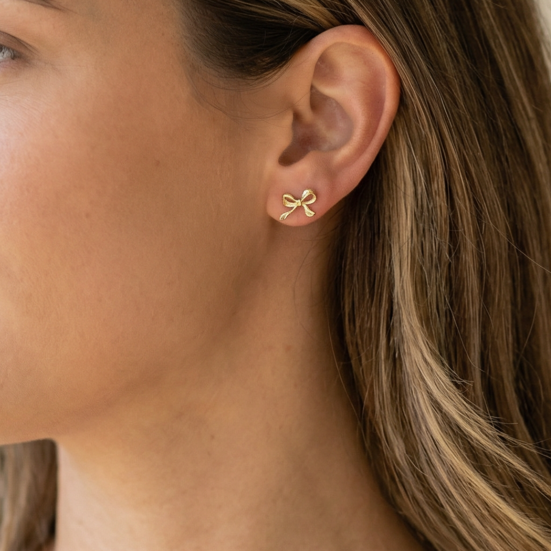 Close-up of a person wearing a gold bow-shaped earring.