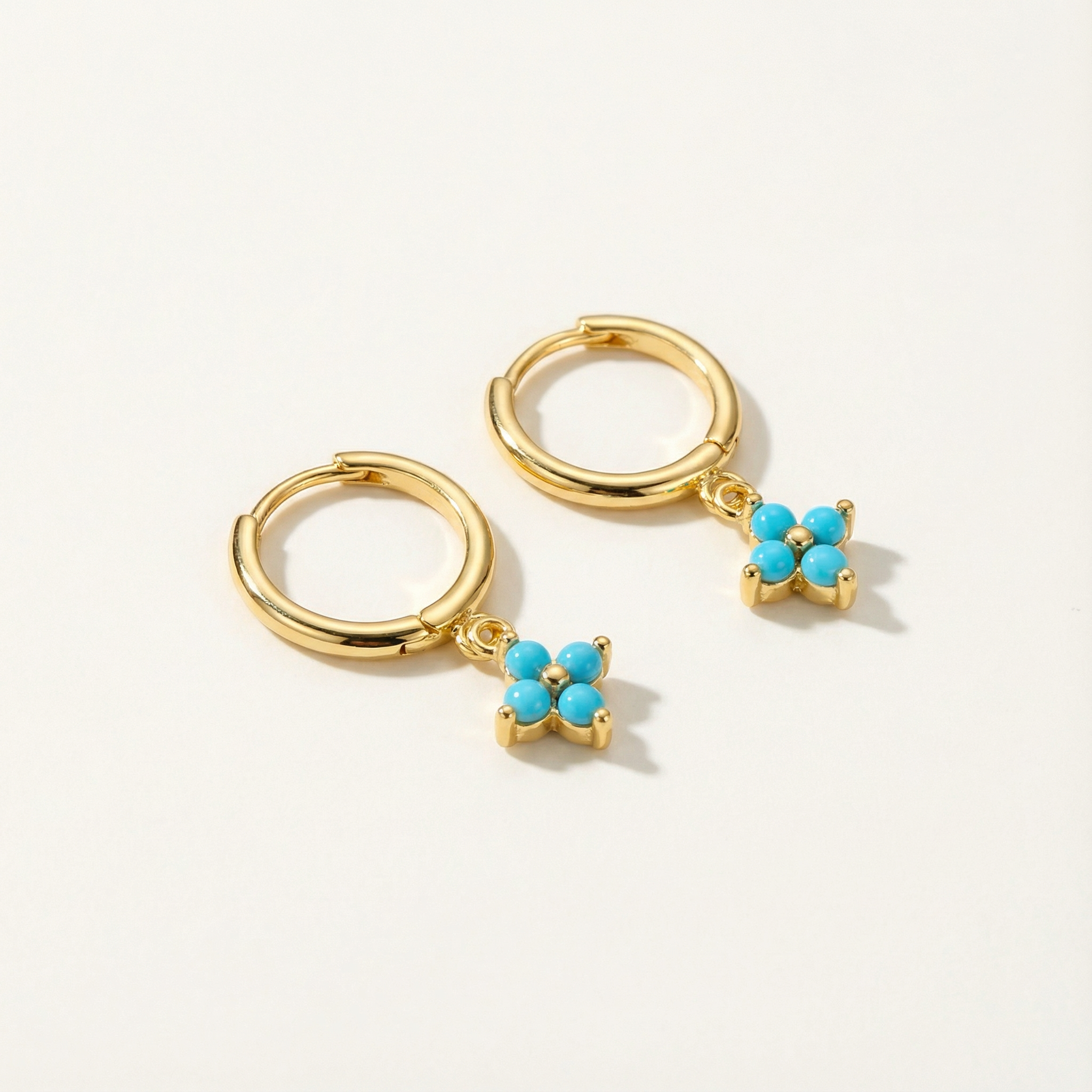 Gold hoop earrings with turquoise flower charms on a light gray background