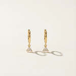Gold hoop earrings with diamond-like stones on a light beige background