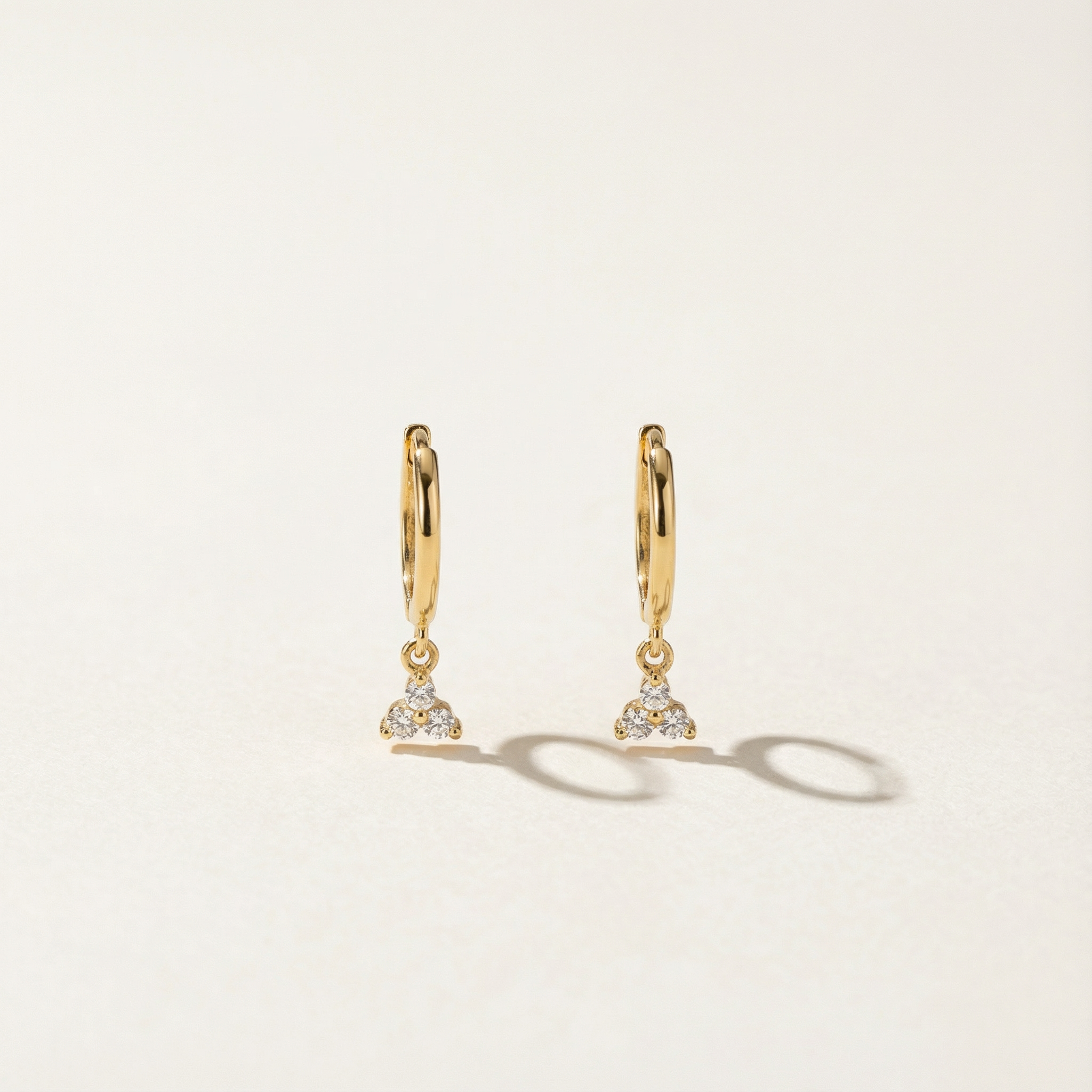 Gold hoop earrings with diamond-like stones on a light beige background