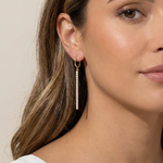 Close-up of a woman wearing gold dangle earrings with a neutral background