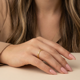 Hand wearing a gold dainty ring with pink nail polish on a neutral background