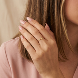 Close-up of a hand wearing a gold ring with a heart design, holding hair against a neutral background.