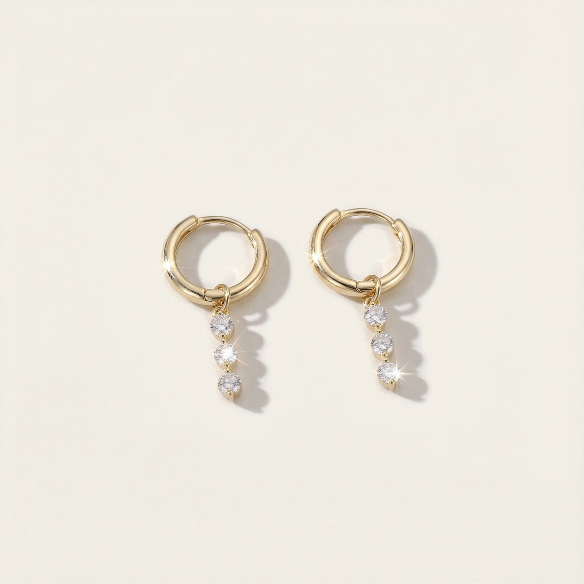 Gold hoop earrings with small crystals on a light beige background