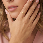 Close-up of a hand wearing a gold heart-shaped ring with a blurred background