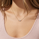 Gold necklace with a small pendant on a person wearing a pink top.