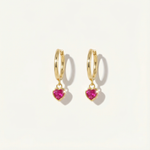 Gold hoop earrings with heart-shaped pink gemstones on a light beige background