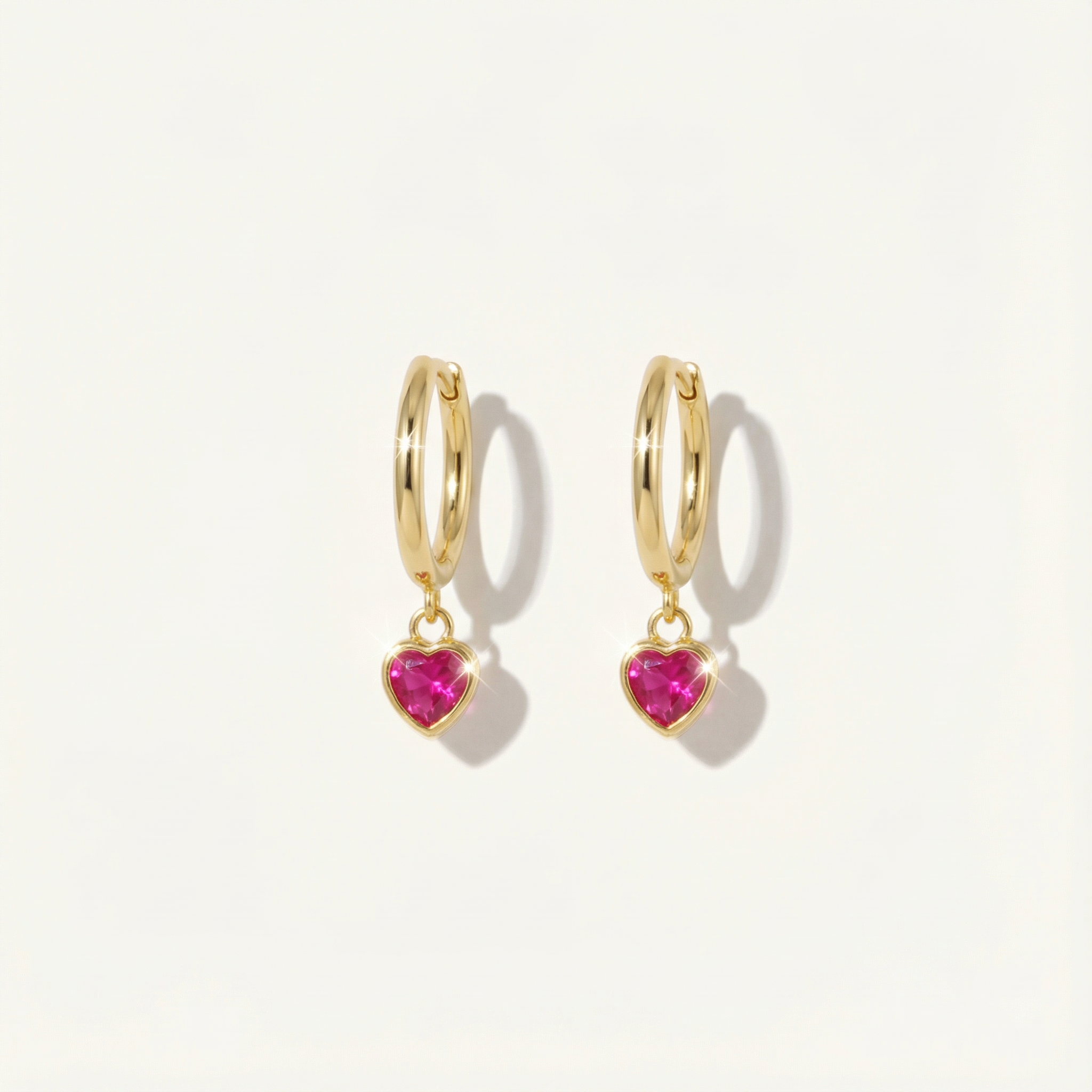 Gold hoop earrings with heart-shaped pink gemstones on a light beige background