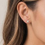 Close-up of an ear wearing an opal stud earring with a neutral background