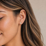 Close-up of a woman's ear wearing a gold opal stud earring with a neutral background