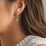 Close-up of a woman wearing a gold hoop earring with a blue gemstone.
