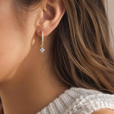 Close-up of a woman wearing a gold hoop earring with a blue gemstone.