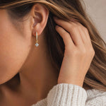 Close-up of a person wearing a gold earring with a small blue gemstone.