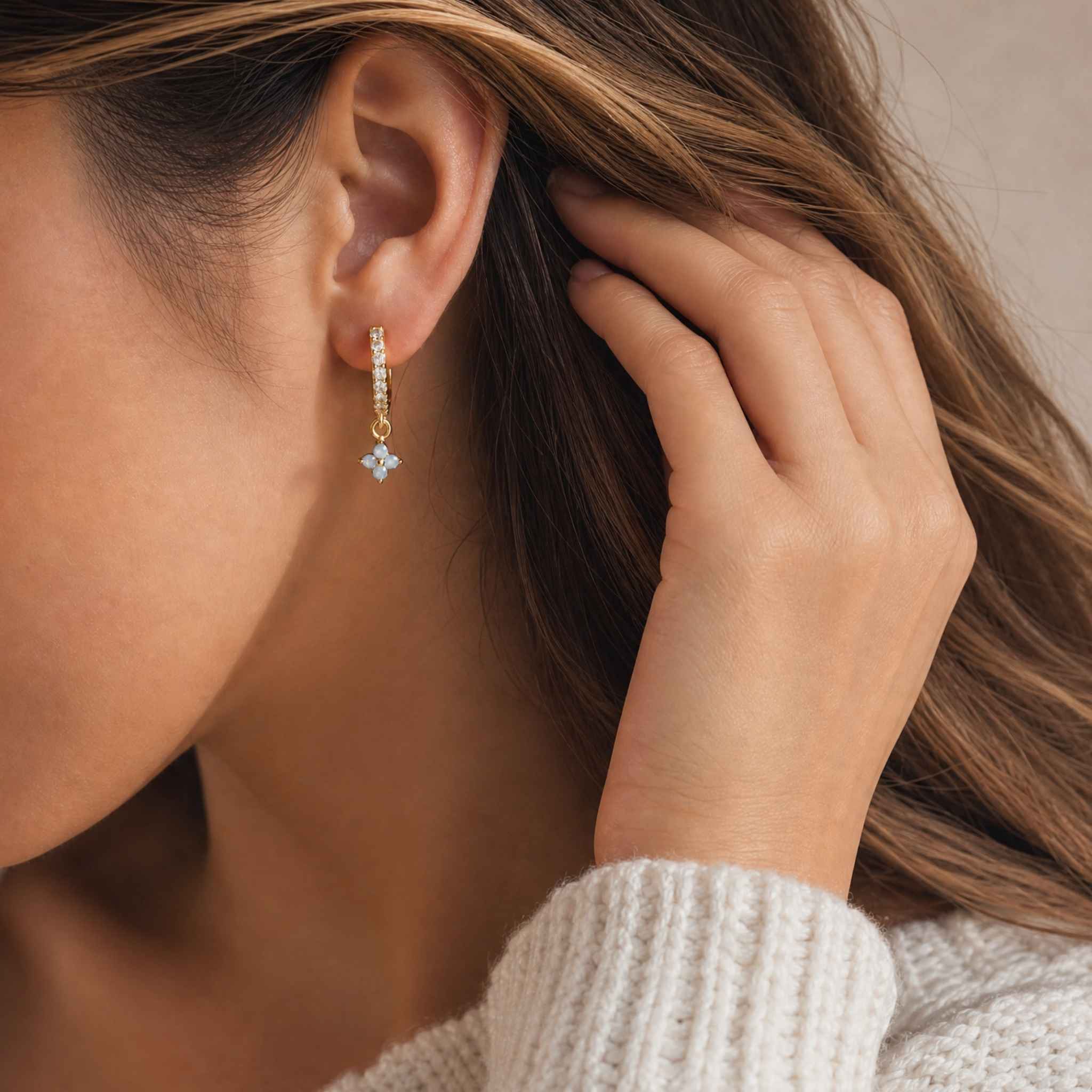 Close-up of a person wearing a gold earring with a small blue gemstone.