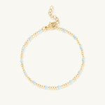 Gold bracelet with small blue beads on a white background
