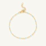 Gold bracelet with small blue beads on a white background
