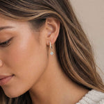 Close-up of a woman wearing a gold huggie earring with a blue gemstone.