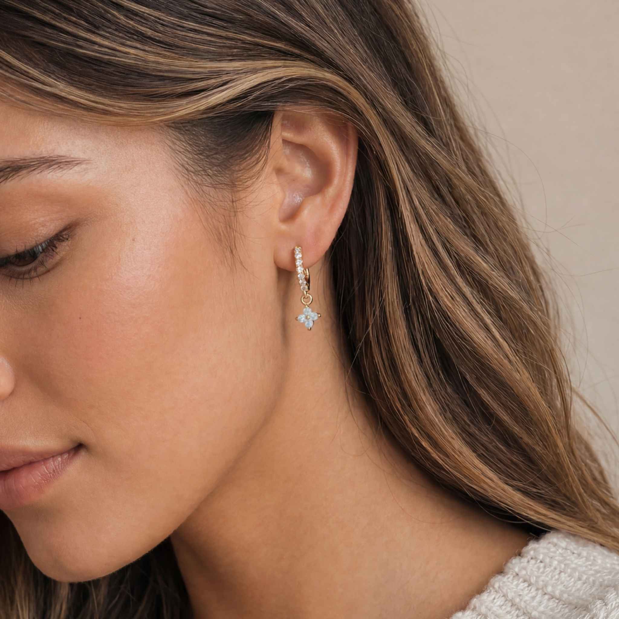 Close-up of a woman wearing a gold huggie earring with a blue gemstone.