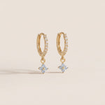 Gold hoop earrings with flower-shaped charms on a beige background