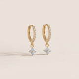 Gold hoop earrings with flower-shaped charms on a beige background