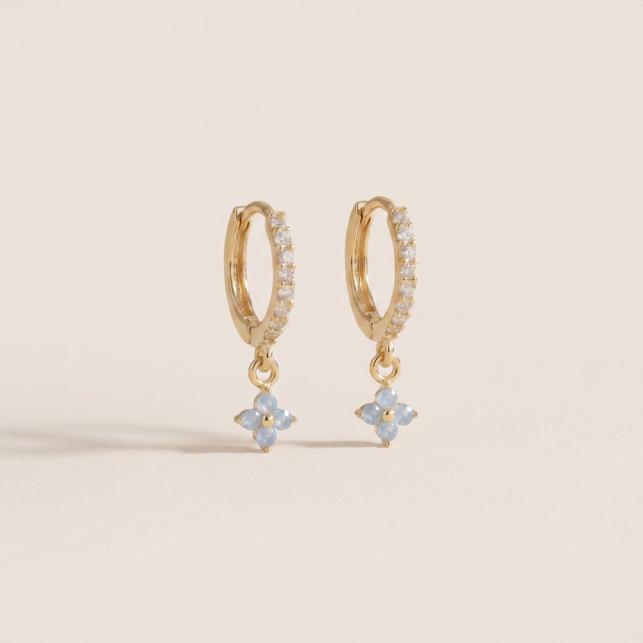 Gold hoop earrings with flower-shaped charms on a beige background