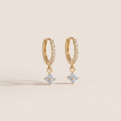 Gold hoop earrings with flower-shaped charms on a beige background
