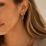 Close-up of a woman wearing small gold hoop earrings with a beaded texture, shown on her ear against her hair and skin.