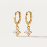 Gold hoop earrings with opal flower drops on a light beige background