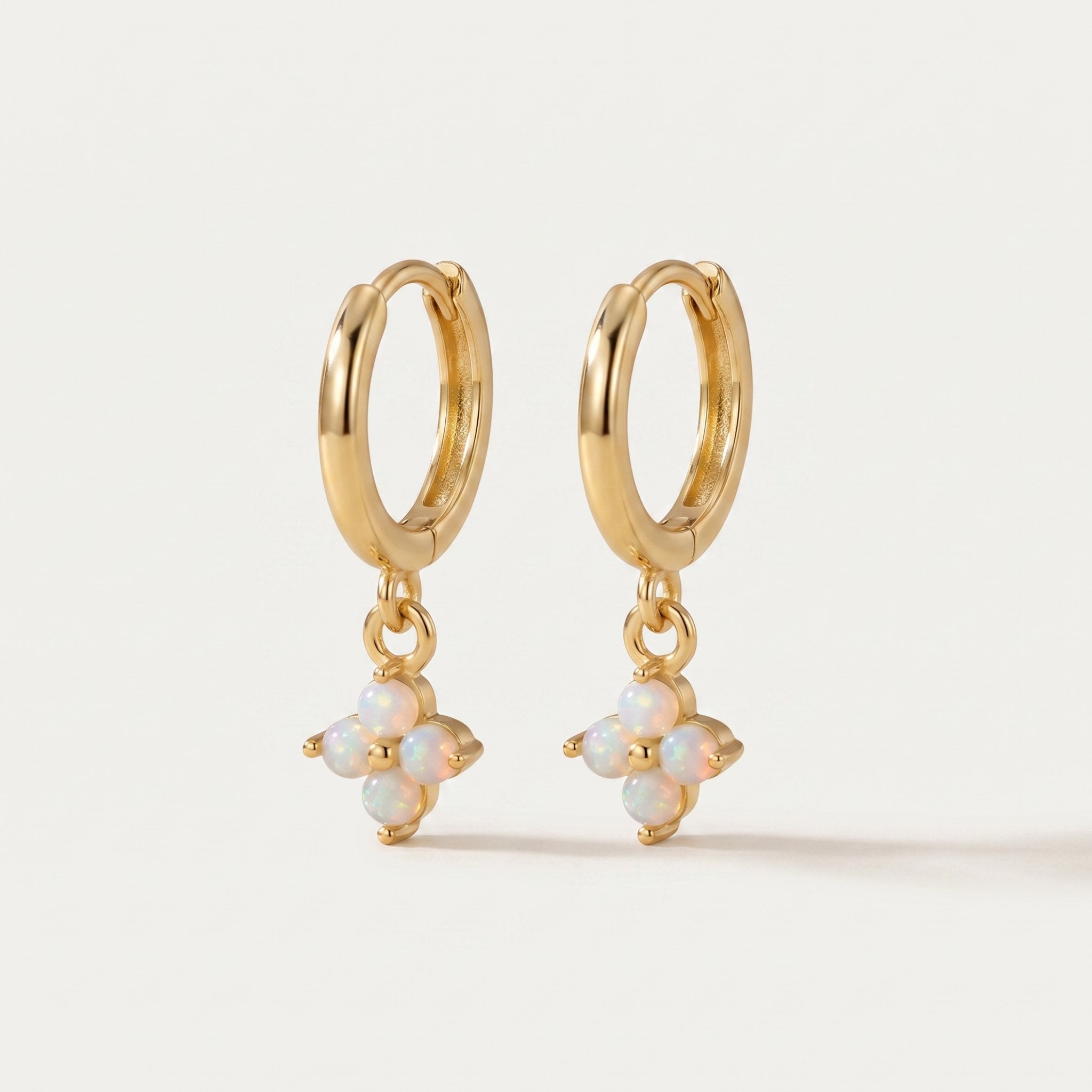 Gold hoop earrings with opal flower drops on a light beige background