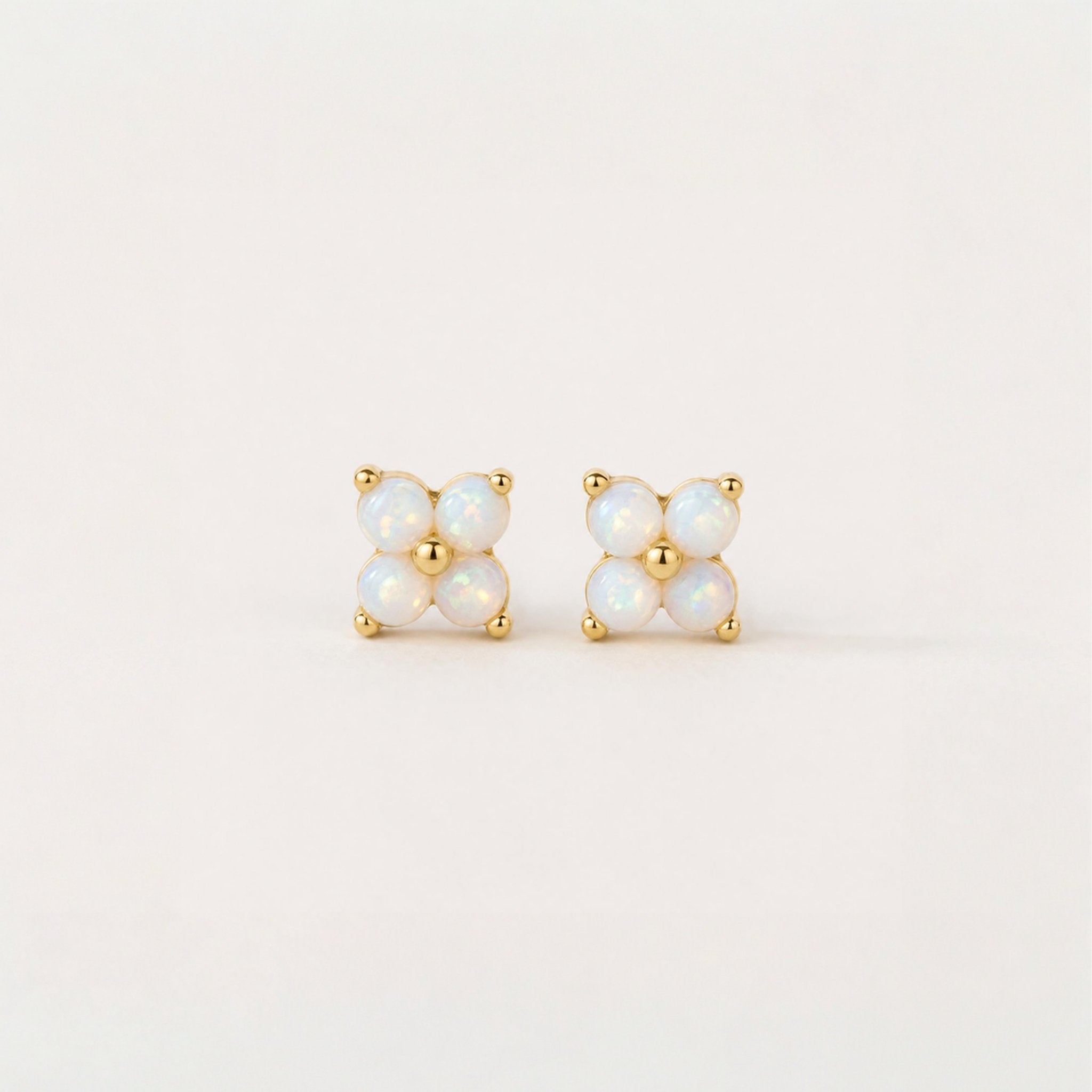 Pair of gold and opal stud earrings on a light beige background