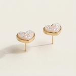Heart-shaped earrings with pink gemstones on a beige background