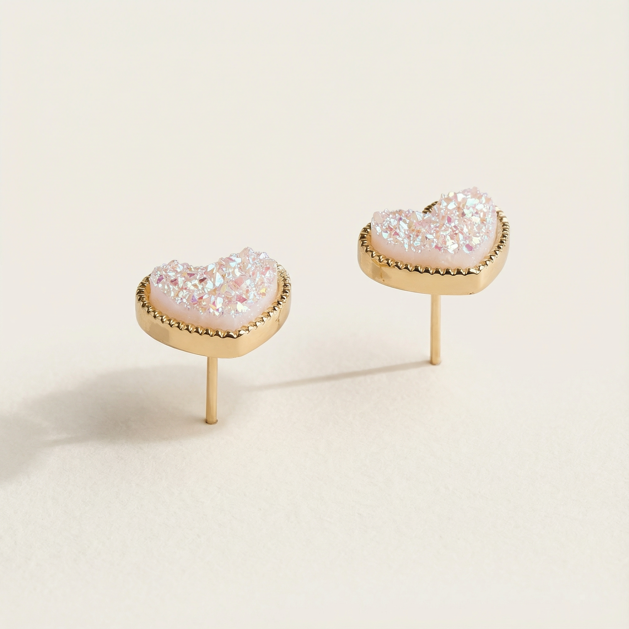 Heart-shaped earrings with pink gemstones on a beige background