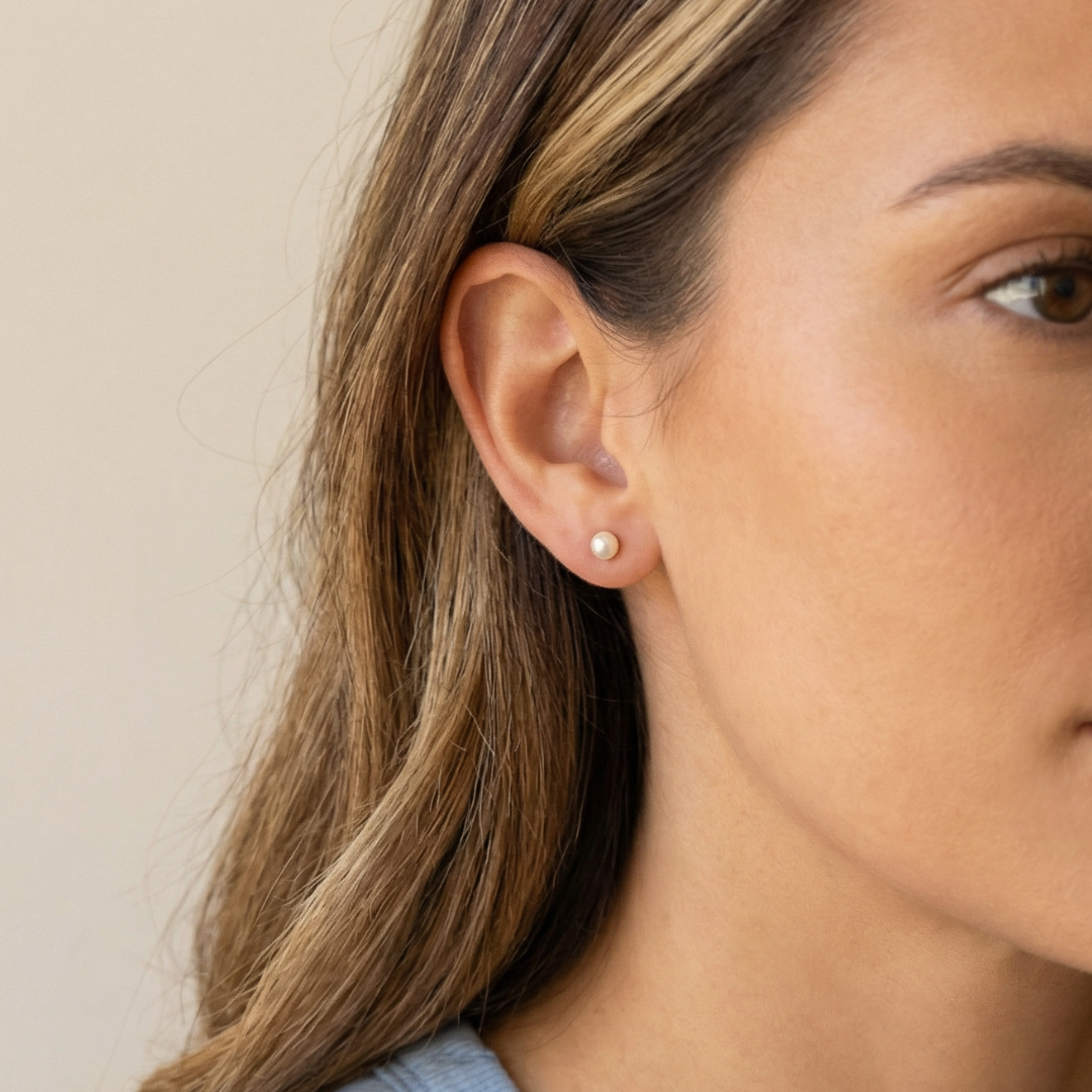 Close-up of a woman wearing a dainty pearl earring with a neutral background