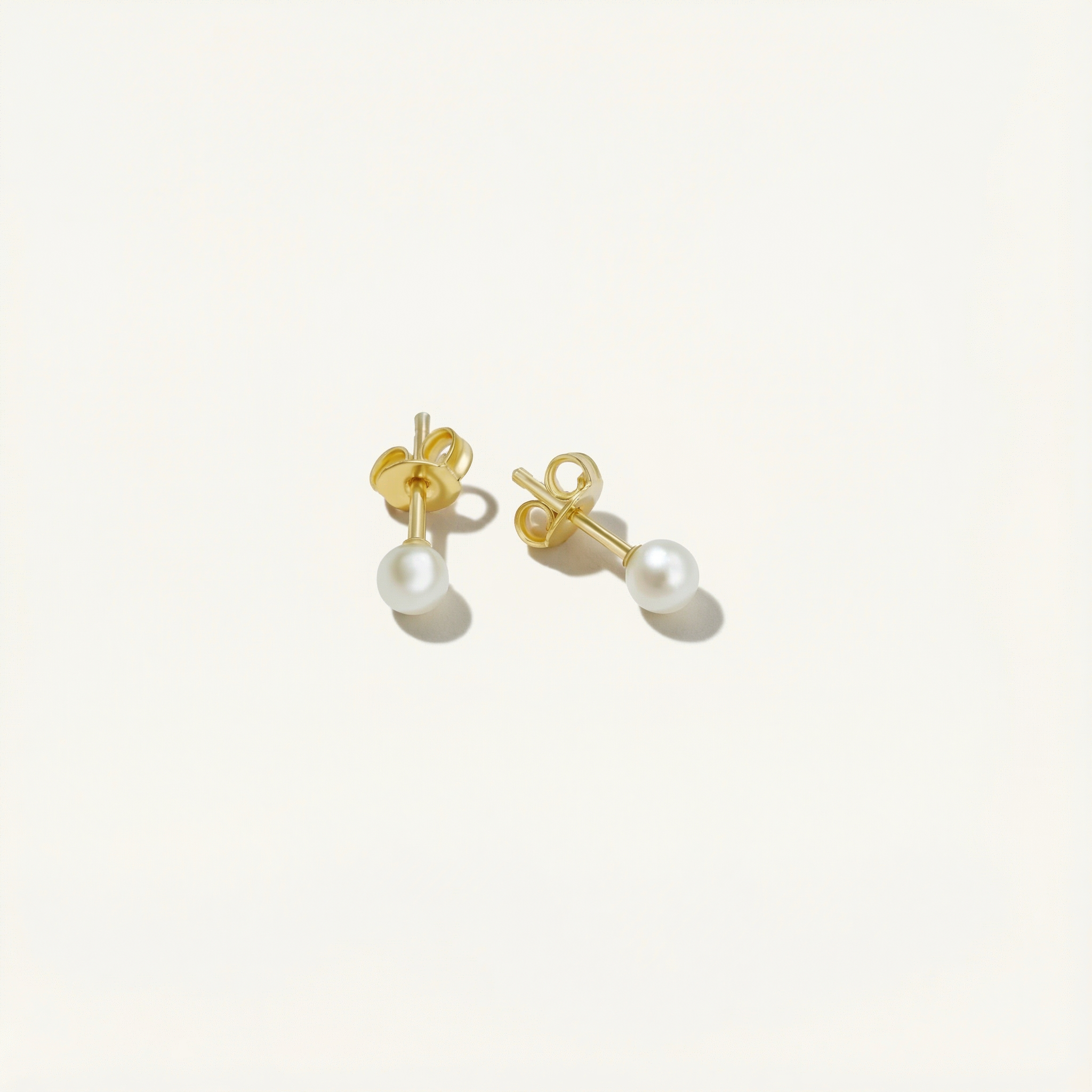 Pair of dainty pearl earrings with gold studs on a white background