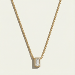 Gold necklace with a rectangular diamond pendant on a light beige background