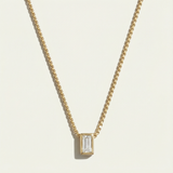 Gold necklace with a rectangular diamond pendant on a light beige background