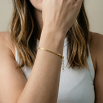 Close-up of a person wearing a gold bracelet on a neutral background