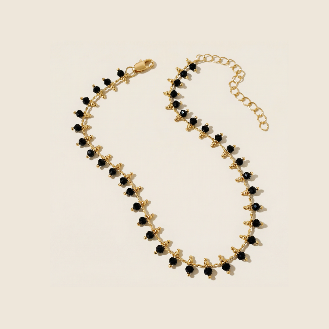 Gold dainty bracelet with black beads on a beige background