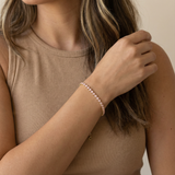 Woman wearing a pink tennis bracelet on her wrist with a neutral background