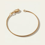 Gold snake chain bracelet on a light beige background