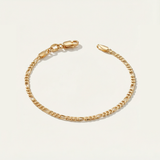 Gold figaro bracelet on a light beige background