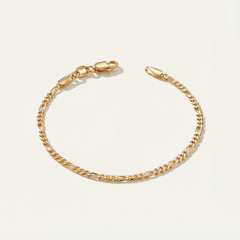 Gold figaro bracelet on a light beige background