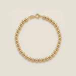 Gold beaded bracelet on a beige background