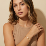 Woman wearing a beige sleeveless top  and a dainty gold bracelet against a beige background