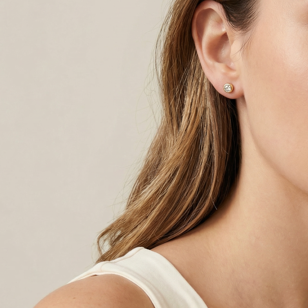 Close-up of a person wearing a gold dainty earring with a beige background