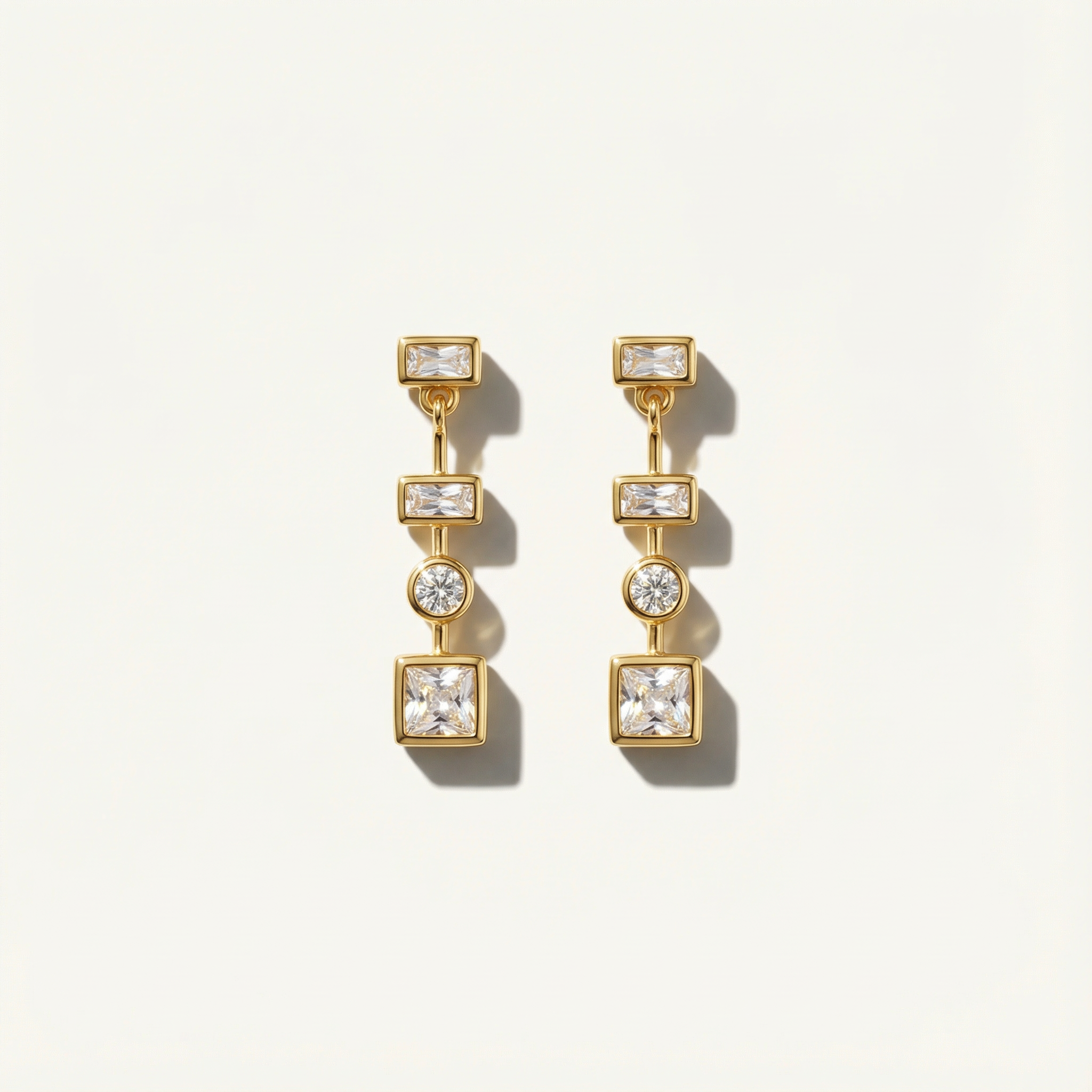 Gold earrings with square and round gemstones on a light gray background