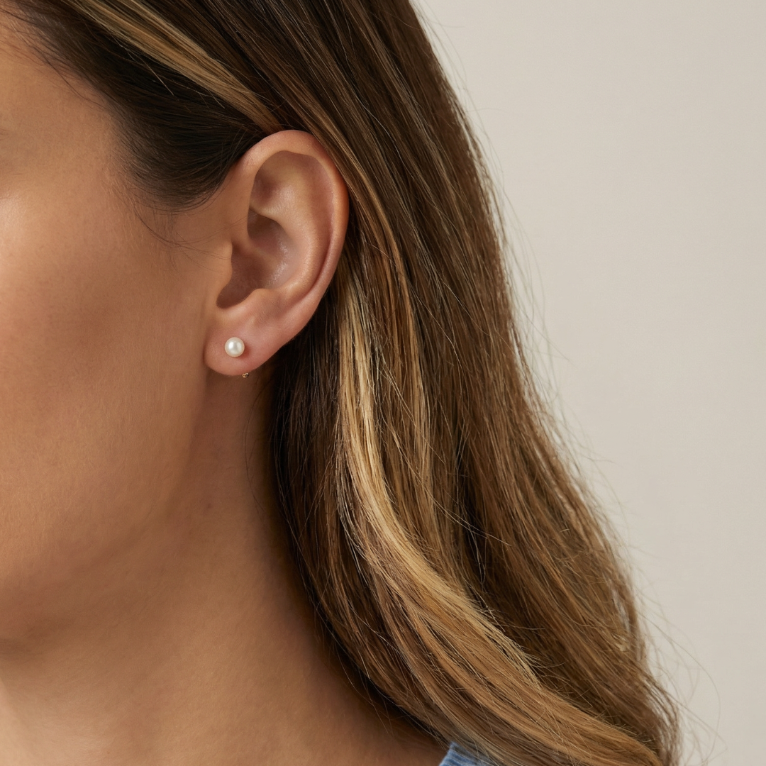 Close-up of a person wearing a pearl earring with a neutral background