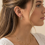 Close-up of a woman wearing gold hoop earrings and a delicate necklace against a neutral background