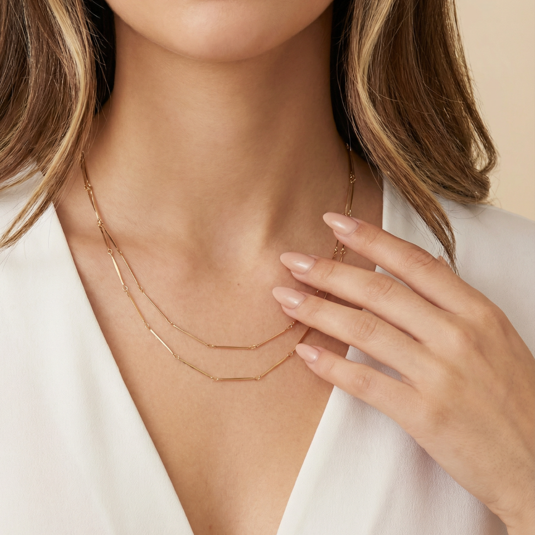 Close-up of a woman wearing a delicate 18k gold necklace with a neutral background
